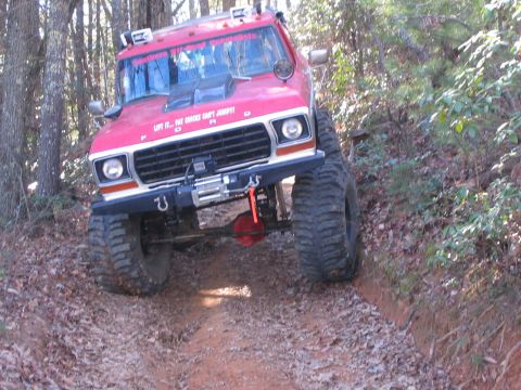 1979 Ford Bronco - This modified Ford truck is navigating a wooded trail with steep inclines and loose dirt.