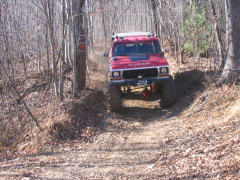 1979 Ford Bronco - A red 1979 Ford Bronco navigates a steep, dirt path through a wooded area, kicking up dust.