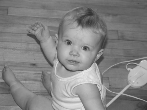 1990 Ford Bronco - A baby sits on a wooden floor, looking up with an open mouth and one arm raised.