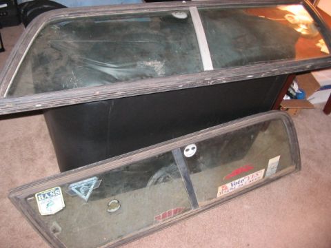 1991 Ford Bronco - Two vehicle windows are shown, one resting on top of the other. The lower window has multiple stickers applied to its surface.