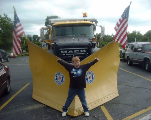 1985 Ford F-150 - Child poses in front of a Mack snow plow truck decorated with American flags.