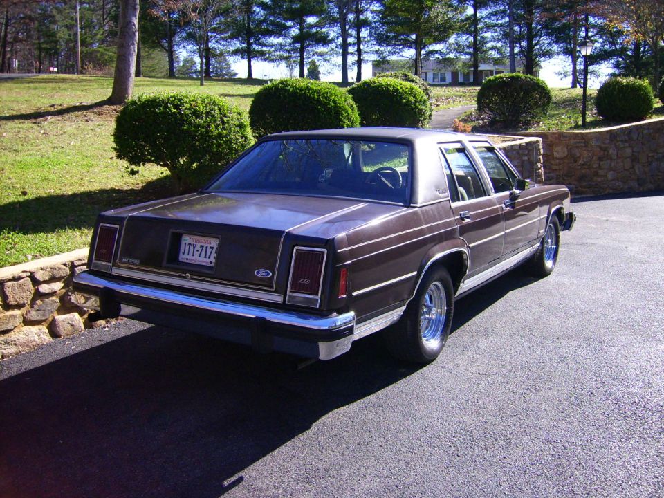 Brown sedan parked on asphalt, rear view. Chrome bumper, rectangular taillights, and a license plate are visible