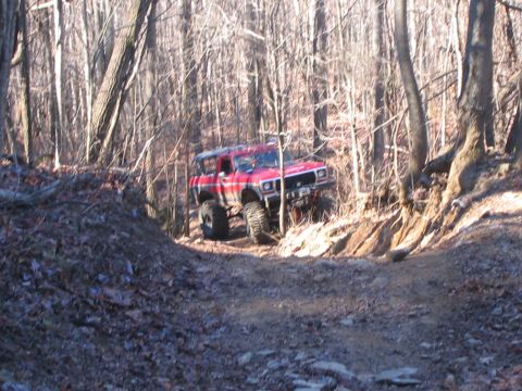 1979 Ford Bronco - A red Jeep Cherokee XJ navigates a wooded trail with significant ground clearance.