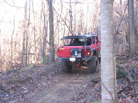 1979 Ford Bronco - A modified red SUV navigates a wooded trail with significant ground clearance and off-road tires.