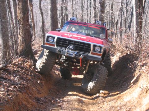 1979 Ford Bronco - A red lifted Ford 4x4 crawls down a rutted dirt trail through bare winter woods, articulating over the off-camber bank on huge mud-terrain…