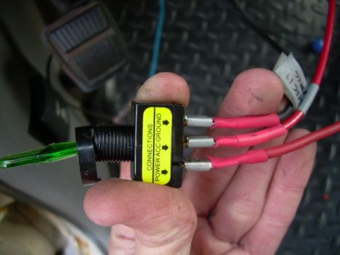 1988 Ford Bronco - An aftermarket toggle switch with wiring is held in hand, with text visible on the switch.