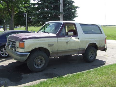 1990 Ford Bronco - This is a side view of a tan and maroon Ford Bronco, showing its off-road tires and aftermarket wheels.