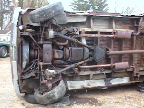1993 Ford Bronco - The underside of an overturned vehicle is shown, revealing its drivetrain and exhaust system. Another vehicle is visible in the background.