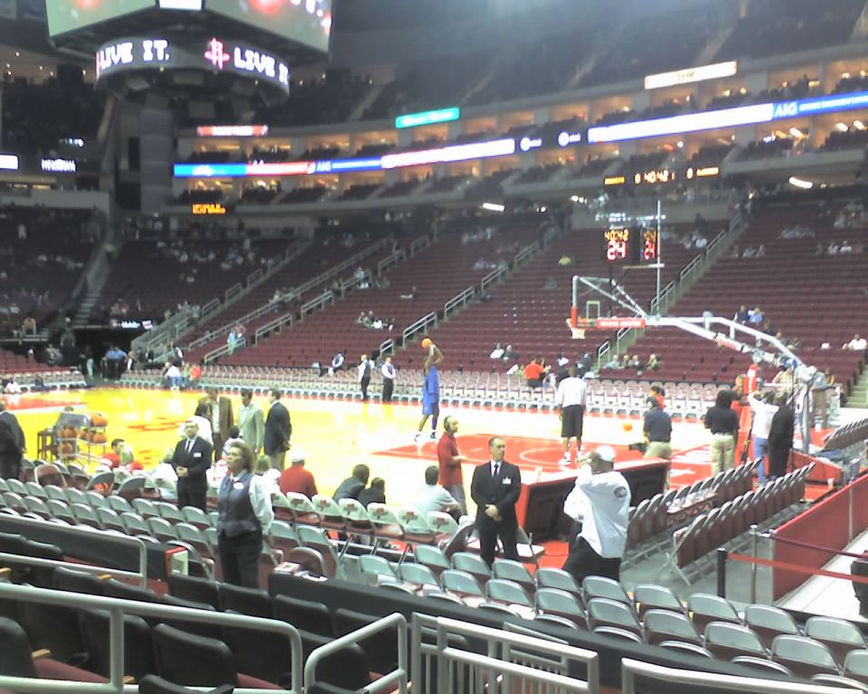 Basketball game in progress with players on court and spectators in stands. Scoreboard visible