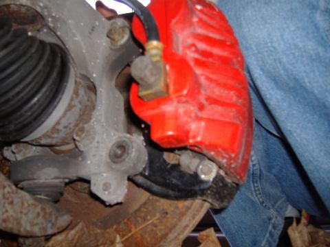 1998 Ford Taurus - Close-up view of a red brake caliper and associated suspension components, with a person's leg in denim jeans in the background.