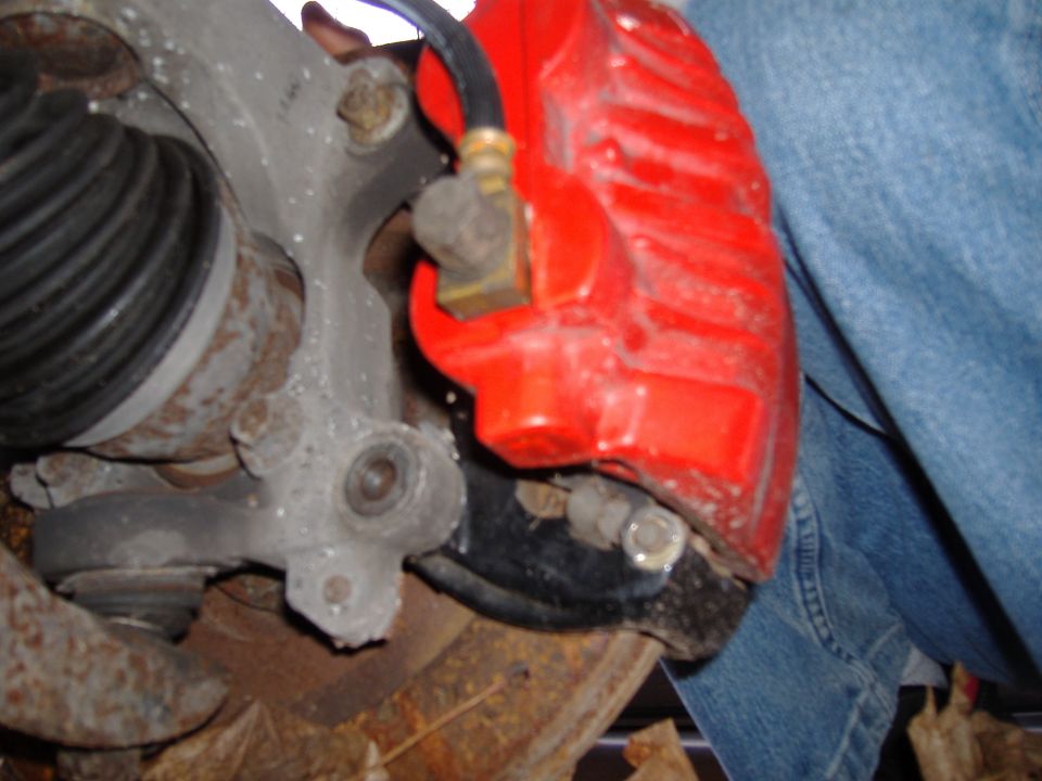Red brake caliper and suspension parts on a vehicle, with a person in jeans visible