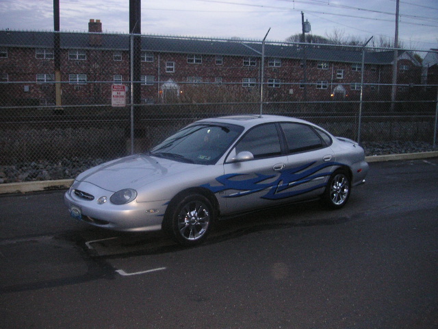 Silver sedan with blue flame decals on the side, parked in front of a brick building