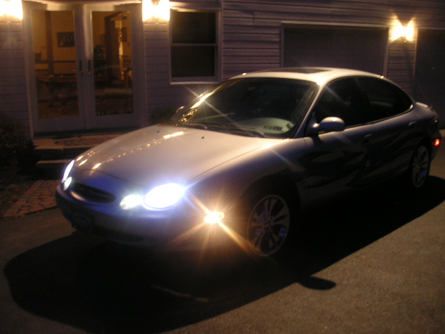 1999 Ford Taurus parked in front of a house at night, headlights on