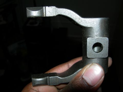1992 Ford Taurus - A metal automotive part is held in a hand against a dark background.