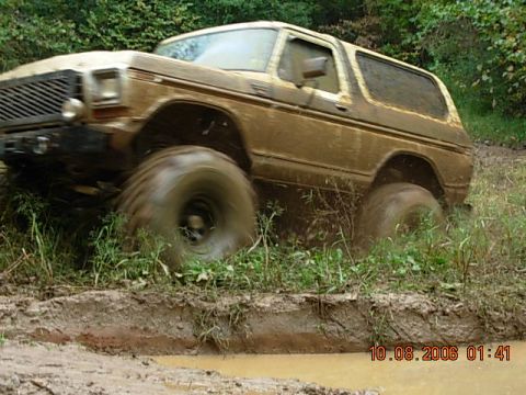 1992 Ford Mustang - A muddy brown 1978 Ford Bronco navigates a challenging off-road course, kicking up mud and water.