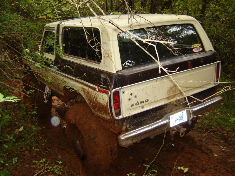 1978 Ford Bronco stuck in mud on a trail, rear view. Mud covers the tires and lower body