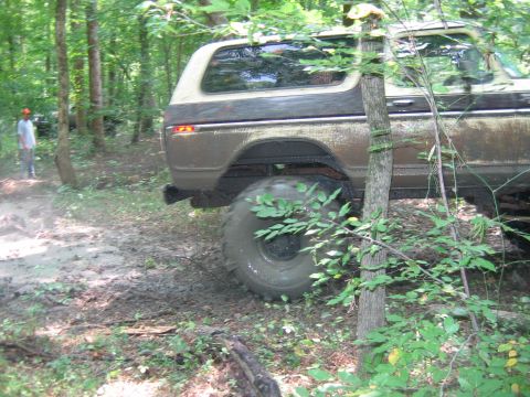 1992 Ford Mustang - A muddy brown and tan Ford Bronco with large off-road tires is seen from the rear in a wooded area.