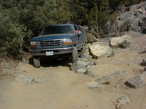 1987 Ford Bronco - This blue Ford Bronco is tackling a challenging rocky trail, demonstrating its off-road capabilities.