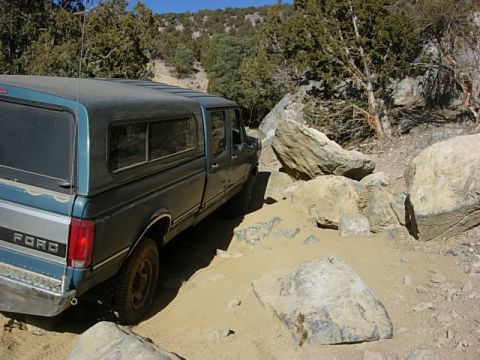 1987 Ford Bronco - A 1987 Ford pickup truck with a camper shell drives through a challenging rocky and sandy off-road path.