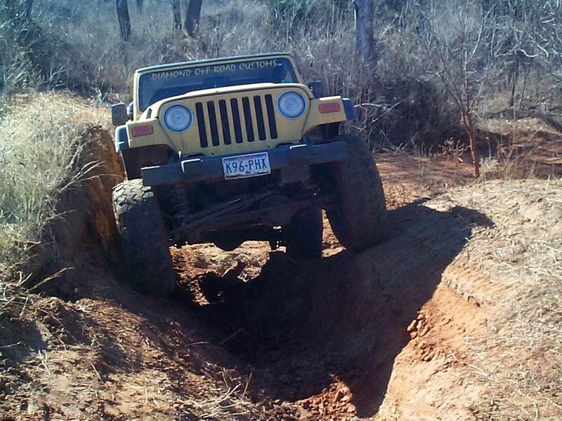 Front of tan Jeep Wrangler with Texas plate crawling down into a deep dirt rut
