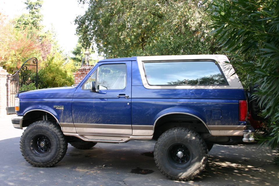Blue Ford Bronco parked on a driveway, side view. It has a tan trim and a removable top