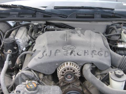 2000 Ford Crown Victoria - The engine bay shows a cover with "SUPERCHARGED" written on it, along with the alternator and various hoses.