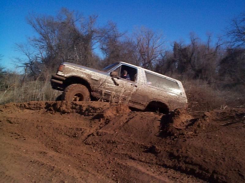 Mud-covered full-size Bronco descending a clay slope, driver visible through window