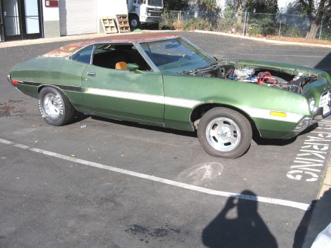 1972 Ford Ranchero - A green coupe sits in a parking lot with its hood open, revealing the engine compartment.