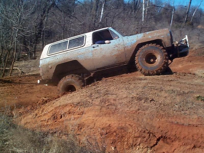 Mud-coated square-body Chevy Blazer climbing a red dirt hill on big tires