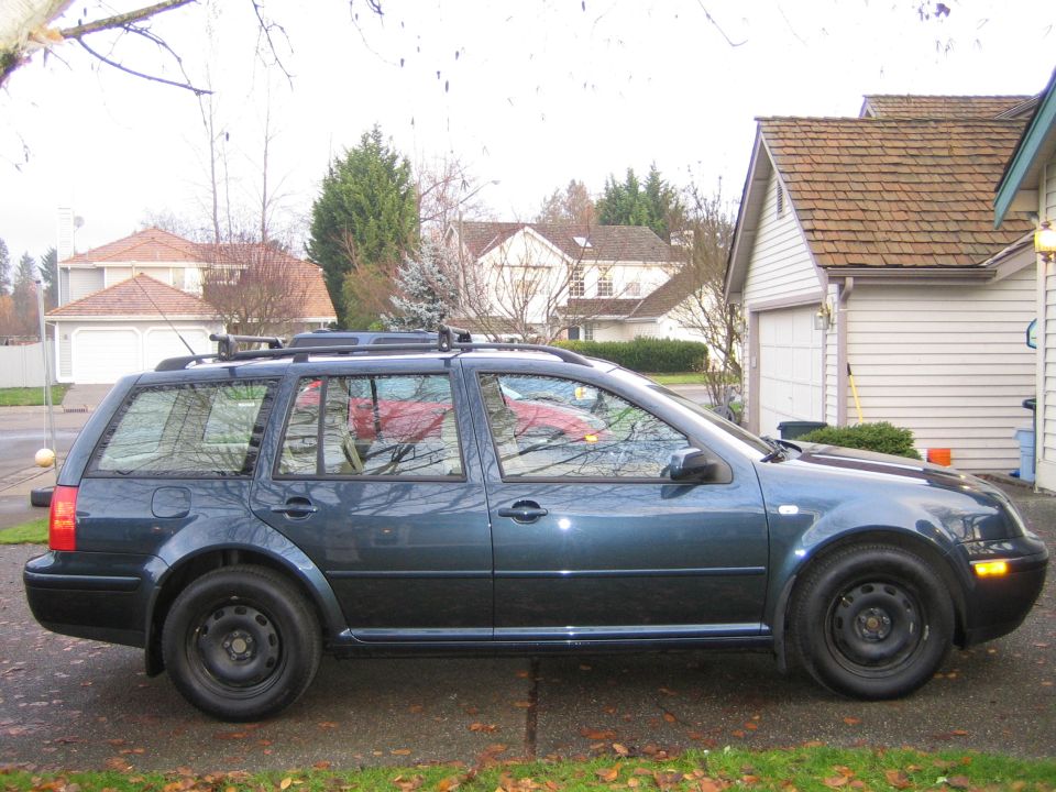 Dark blue-green VW Jetta wagon with roof rack and black steel wheels in a driveway