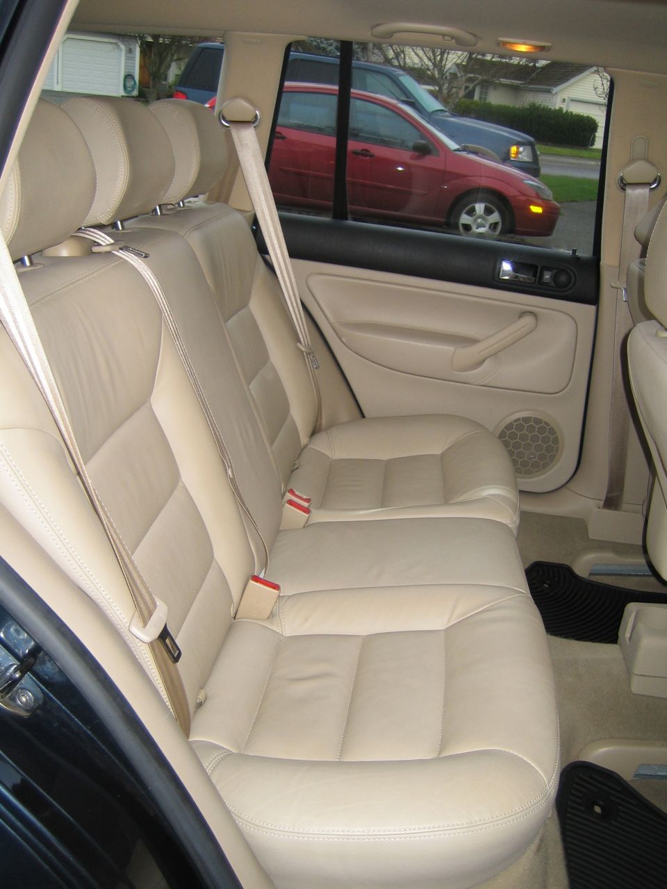 Tan leather rear bench seat of a wagon with red Ford sedan visible through window