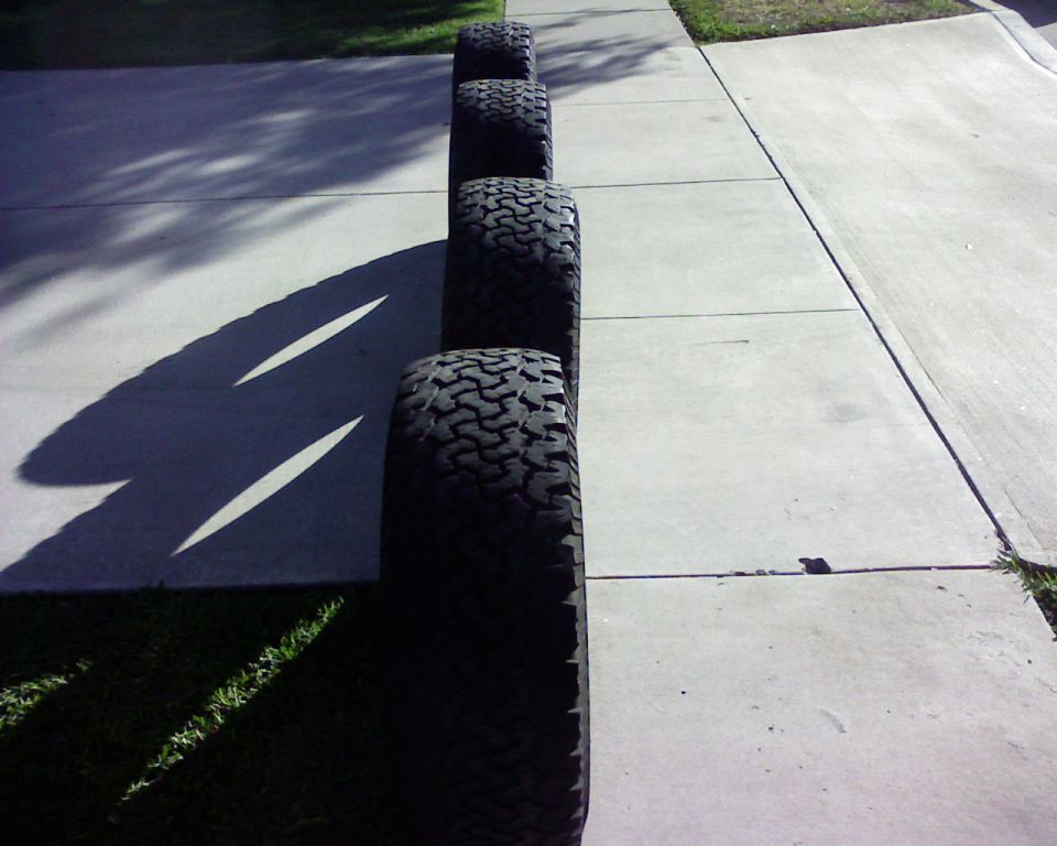 Row of four all-terrain truck tires standing upright on a concrete driveway