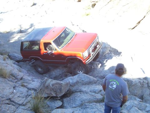 1984 Ford Bronco - A red SUV navigates a rocky trail, with a person observing from the side.