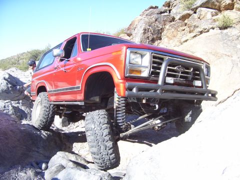 1984 Ford Bronco - Modified red Ford Bronco tackling a challenging rocky trail.