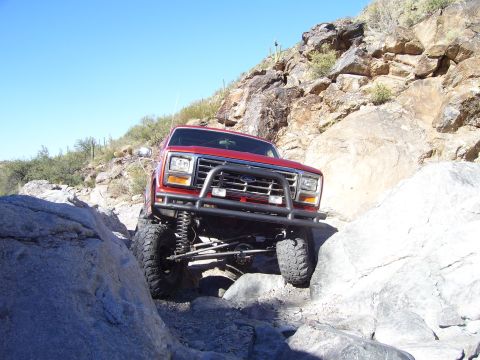 1984 Ford Bronco - This red SUV is navigating a rocky trail under a clear blue sky.