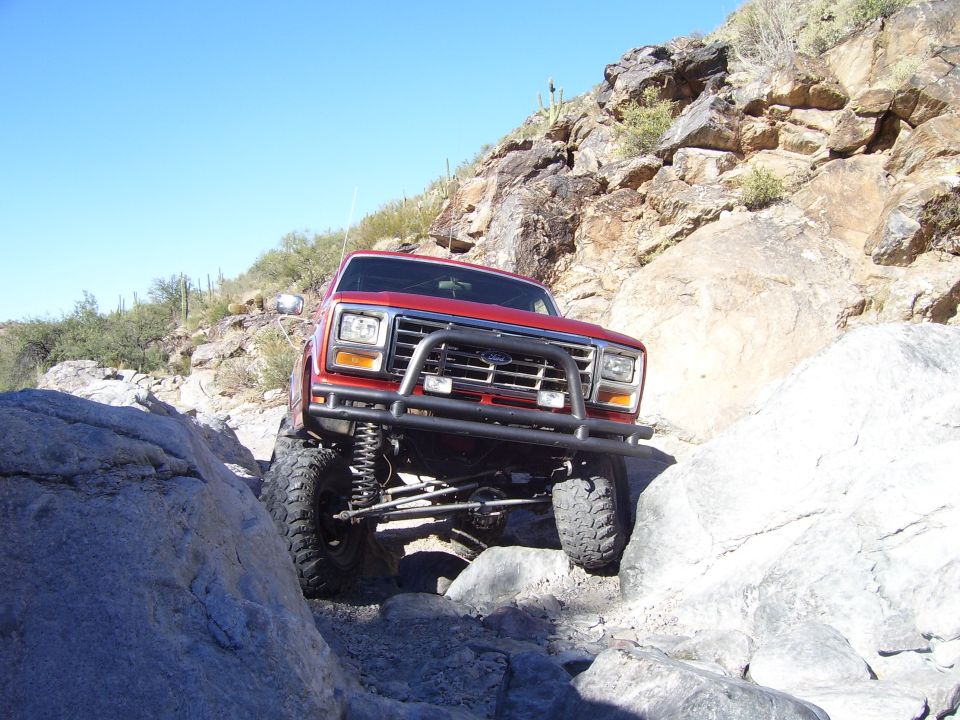 Red SUV with bull bar driving over rocks on a sunny day