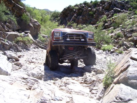 1984 Ford Bronco - This lifted red SUV navigates a challenging rocky trail, its off-road capabilities.