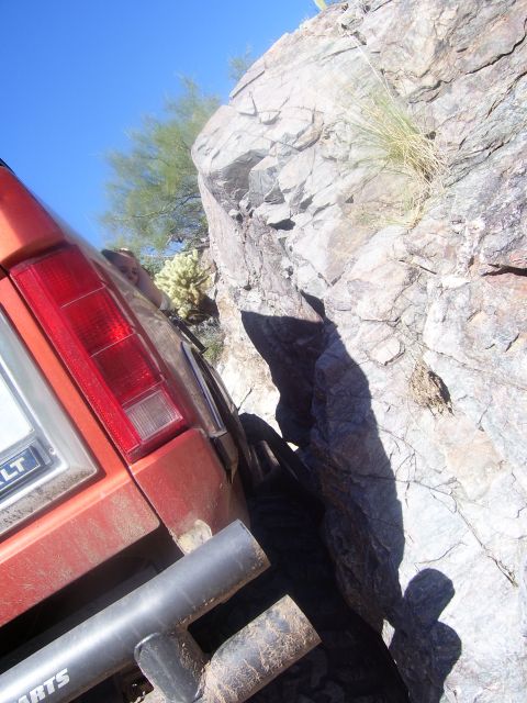 1984 Ford Bronco - Orange SUV navigating a rocky trail, with its rear end close to a large boulder.