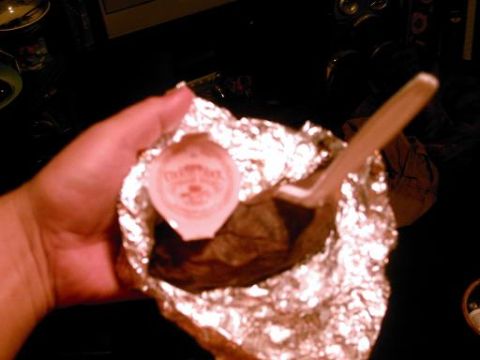 1986 Ford Bronco - A hand holds a foil-wrapped food item with a small condiment cup and a wooden utensil.