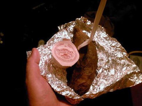1986 Ford Bronco - A hand holds a foil-wrapped baked potato, ready to be eaten with a plastic fork and a side of Country Crock spread.