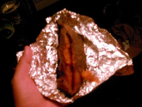 1986 Ford Bronco - Hand holds food item wrapped in crinkled aluminum foil against a dark background.