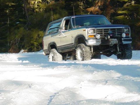 1986 Ford Bronco - A lifted Ford Bronco navigates through a snowy landscape.