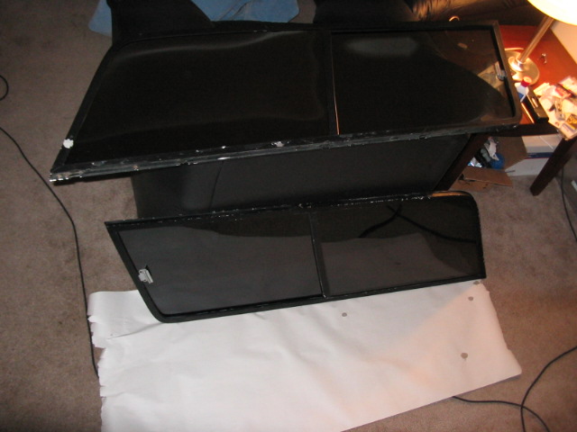 Two black car door windows with frames, one above the other, on a carpeted floor