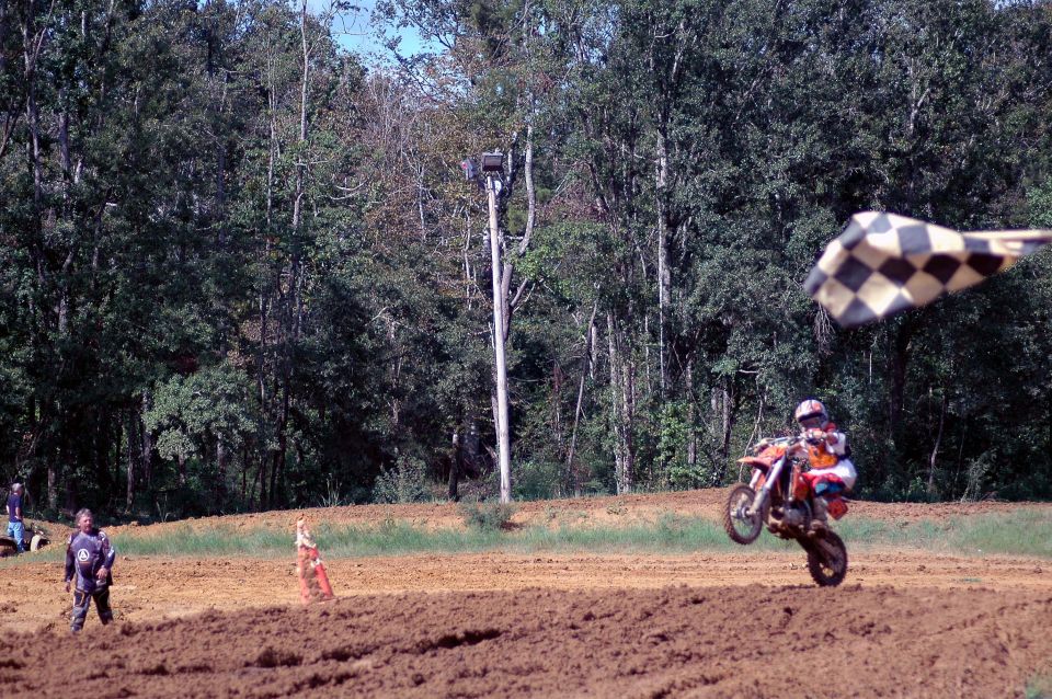 Rider wheelies an orange dirt bike past a checkered flag on a motocross dirt track