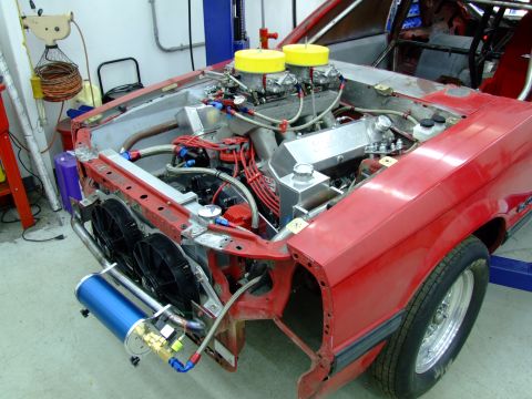 1990 Ford Mustang - Engine bay of a 1990 Ford Mustang, a dual carburetor setup and prominent red body panels.