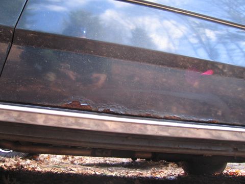 1991 Ford LTD Crown Victoria - Close-up of a car's lower door panel showing significant rust damage and a chrome trim piece.
