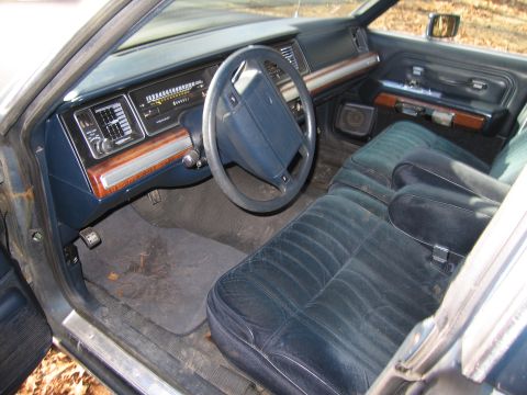 1991 Ford LTD Crown Victoria - Blue cloth interior of a full-size Ford sedan shot through the open driver's door, showing the split bench front seat, column shifter, four…