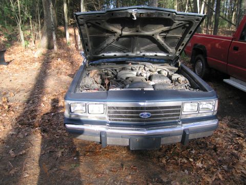 1991 Ford LTD Crown Victoria - The front of a 1991 Ford Crown Victoria LTD is shown with its hood open, revealing the engine compartment.