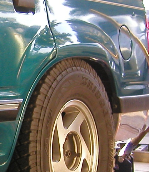 1984 Ford Bronco - Close-up of the rear wheel well of a green SUV, showing the tire, wheel, and fuel door.