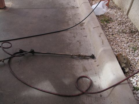 1995 Ford Bronco - A steering linkage component, possibly from a vehicle, lies on a concrete surface with hoses nearby.